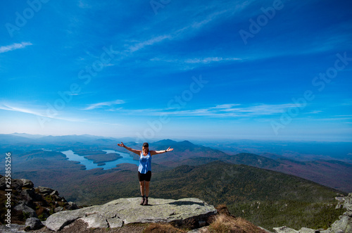 Female hiker standing on the edge of a cliff with her arms out at the summit of Whiteface Mountain