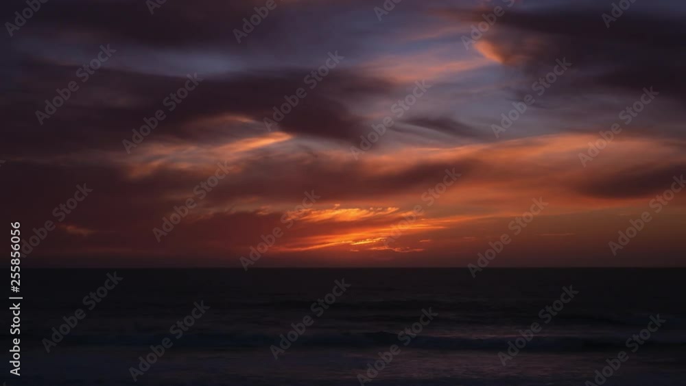 Time lapse, sun dropping below horizon at sunset with blue orange gradient sky and dark clouds Time lapse, sun dropping below horizon at sunset with blue orange gradient sky and dark clouds