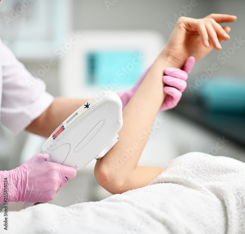 Closeup. Doctor-cosmetician in gloves performes a procedure on patient's hand with medical equipment laser in equiped beauty shop