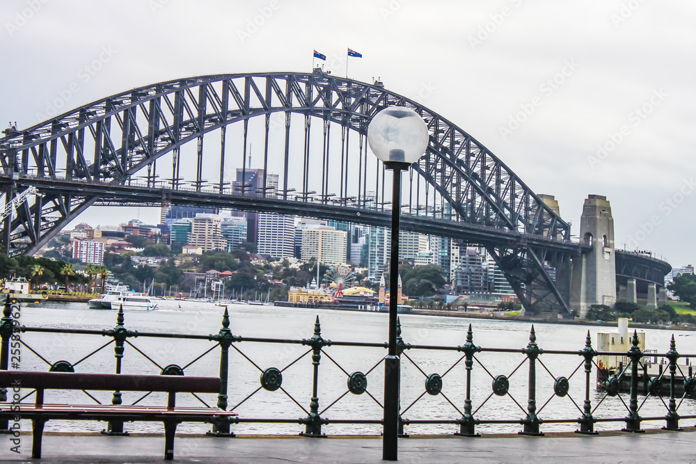 View of Sydney Harbour Bridge from the Circular Quay on a wet morning, with city in the distance and a ferry crossing over View of Sydney Harbour Bridge from the Circular Quay on a wet morning, with city in the distance and a ferry crossing over