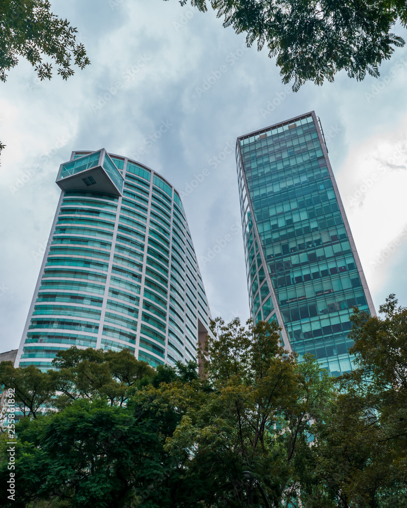 Low angle view of two corporate buildings surrounded by trees on blue sky