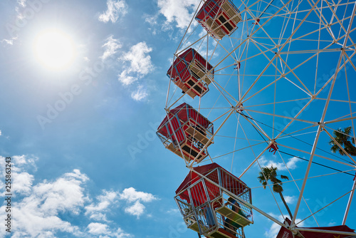 Close view of a colorful Ferris wheel against a vibrant blue sky and palm trees with copy space.