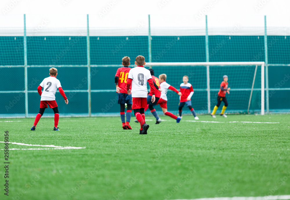 Obraz premium Boys in red white sportswear running on soccer field. Young footballers dribble and kick football ball in game. Training, active lifestyle, sport, children activity concept 