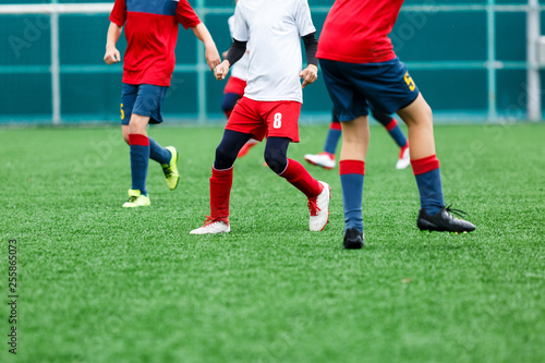 Boys in red white sportswear running on soccer field. Young footballers dribble and kick football ball in game. Training, active lifestyle, sport, children activity concept 