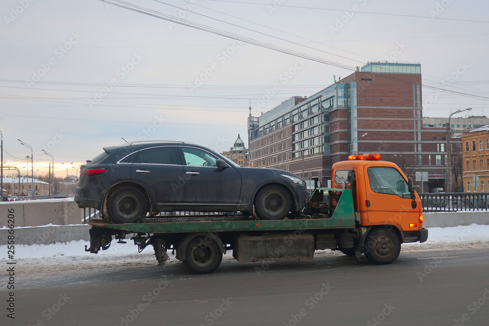 tow truck carrying a black car on a bridge in winter