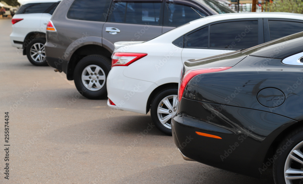 Closeup of back or rear side of black car and other cars parking in parking area in sunny day. 