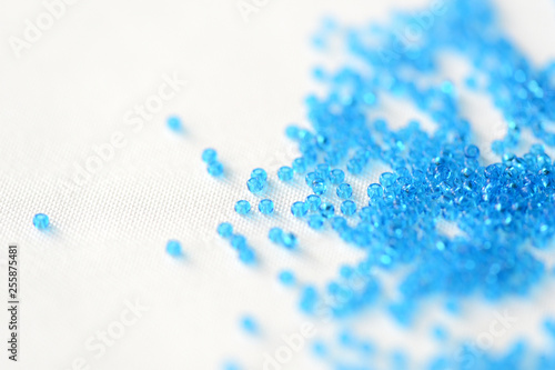 Transparent seed beads blue color scattered on a textile background close up