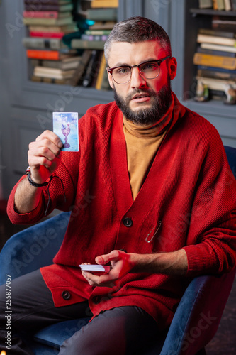 Canvas Print Bearded fortune-teller sitting in armchair and showing divination card