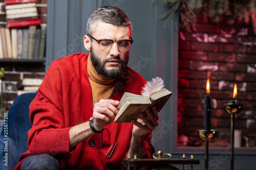 Fotografi Bearded diviner sitting at the table with candles and enjoying self-education