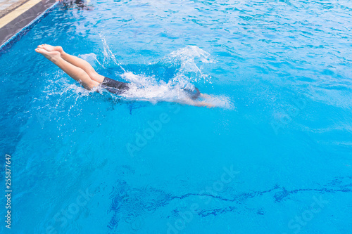 Swimming pool blue color clear water and people enjoying in summer sunny day and top view angle. Jumping. Young woman swimmer in low position on starting block in a swimming pool. 