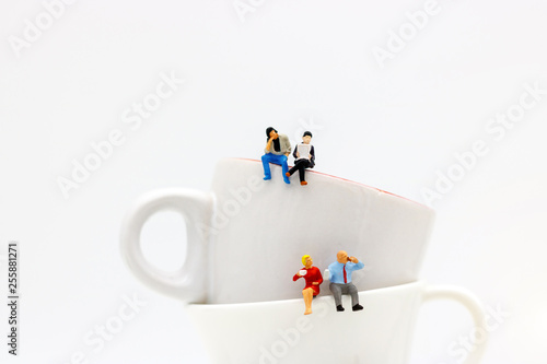 Miniature people: business team sitting on cup of coffee with morning news. Coffee time of business concept.