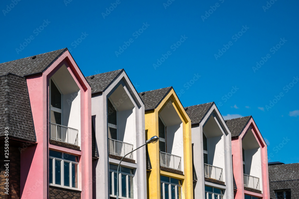 Rows of triangular elements of roofline covered with shingle against blue sky. Colorful pink and yellow house. Copy space