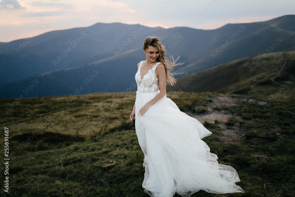 Stylish bride standing on beautiful landscape of mountains on sunset Stylish bride standing on beautiful landscape of mountains on sunset