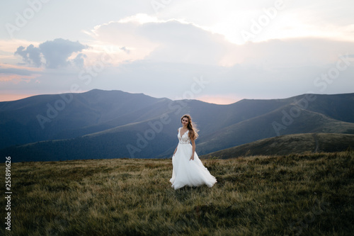 Stylish bride standing on beautiful landscape of mountains on sunset