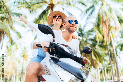 Happy couple going by motorbike under palm trees during their island vacation