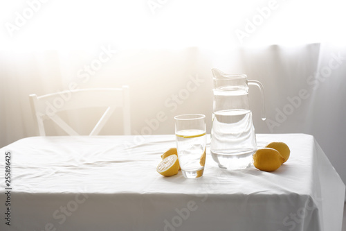 Foto Jug and glass with fresh water and lemons on table