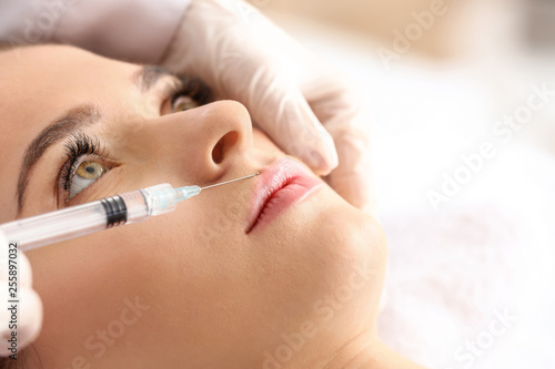 Young woman receiving filler injection in beauty salon