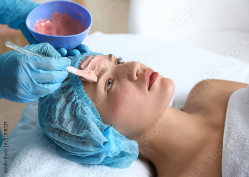 Cosmetologist applying alginate mask on young woman's face in beauty salon photo