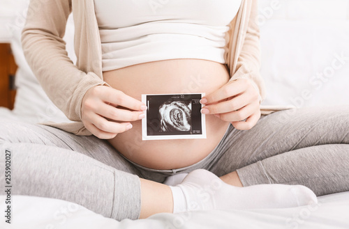 Pregnant woman holding ultrasound photo near belly photo