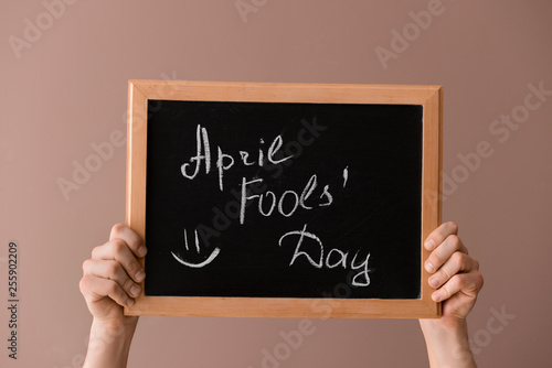 Male hands holding chalkboard with text APRIL FOOL'S DAY on color background