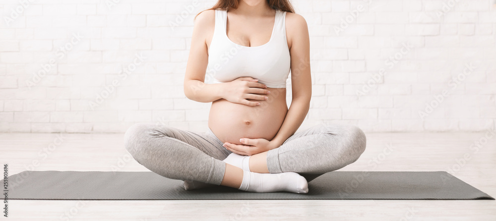 Pregnant woman meditating in lotus position at home - obrazy, fototapety, plakaty 