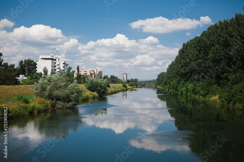 Small calm city river during summer time - Clouds reflecting in the water.