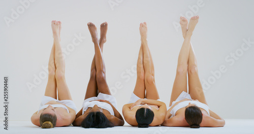 Portrait of beautiful young women of different ethnicities with perfect firm and slim bodies with hairless soft and silky legs crossed isolated on a white background. photo