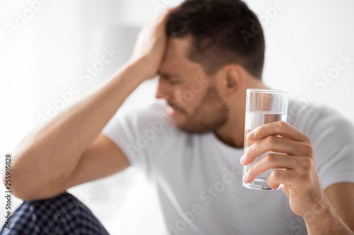 people, health and hydration concept - close up of unhealthy man suffering from hangover with glass of water in morning photo