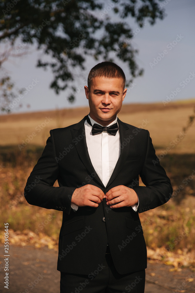 Young man walking in the park. Handsome groom in black suit