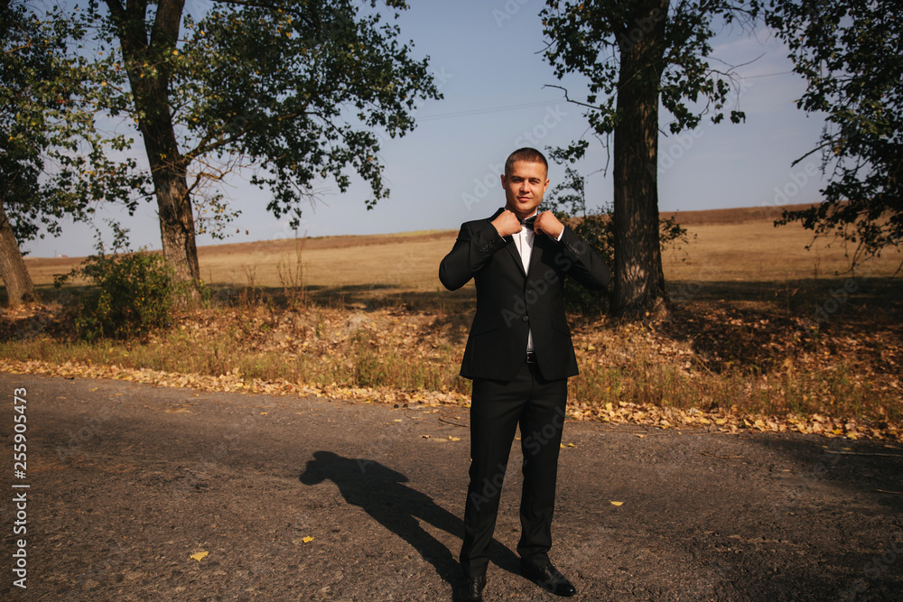 Young man walking in the park. Handsome groom in black suit Young man walking in the park. Handsome groom in black suit