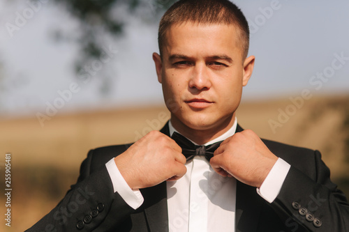 Handsome groomm dressed a tie bow. Wedding day. Man outside photo