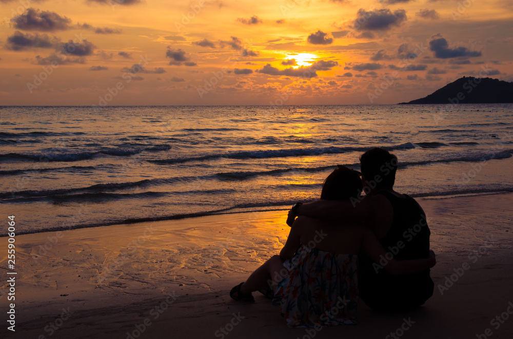 young couple sitting on beach with sunset