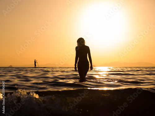 young woman walking in the sea at sunset