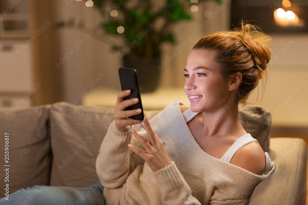 technology and people concept - happy young woman with smartphone at home in evening technology and people concept - happy young woman with smartphone at home in evening