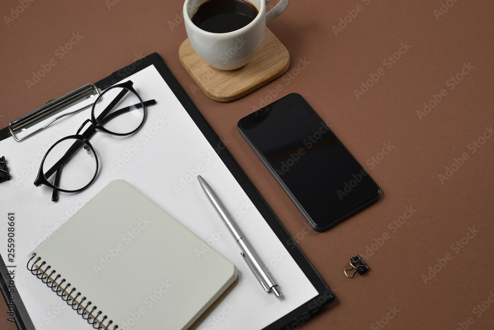Creative flat lay, top view office table desk. Workspace with blank clip board, office supplies, pen, notepad, smartphone, glasses and coffee cup on a brown background. Creative flat lay, top view office table desk. Workspace with blank clip board, office supplies, pen, notepad, smartphone, glasses and coffee cup on a brown background.