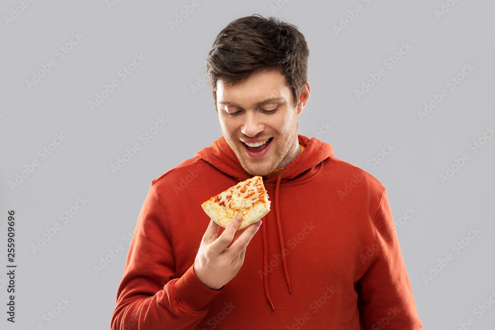 © Syda Productions - fast food and people concept - happy smiling young man in red hoodieeating pizza over grey background