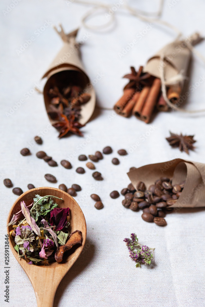 Obraz premium Tea in wooden spoon, coffee cinnamon and anise in craft paper cornets. Rustic rope. Aromatherapy in the kitchen