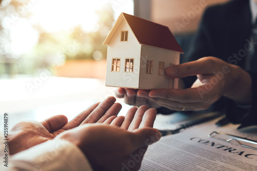 Real estate agent congratulations to new buyer by giving house model to client in the agency office.