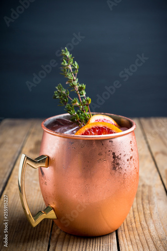 Red oranges cocktail in copper mug (variation of Moscow mule) on the wooden background. Selective focus. Shallow depth of field. photo