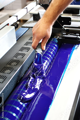 Drukarnia. Drukarz dolewa niebieską farbę drukarską do maszyny.