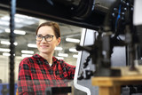 Drukarz. Uśmiechnięta kobieta, pracownik drukarni stoi w hali produkcyjnej na tle nowoczesnych maszyn drukarskich