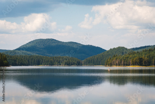 Beautiful summer landscape - calm waters of a lake and a boat. Green forest and mountain in the background. Bulgaria.
