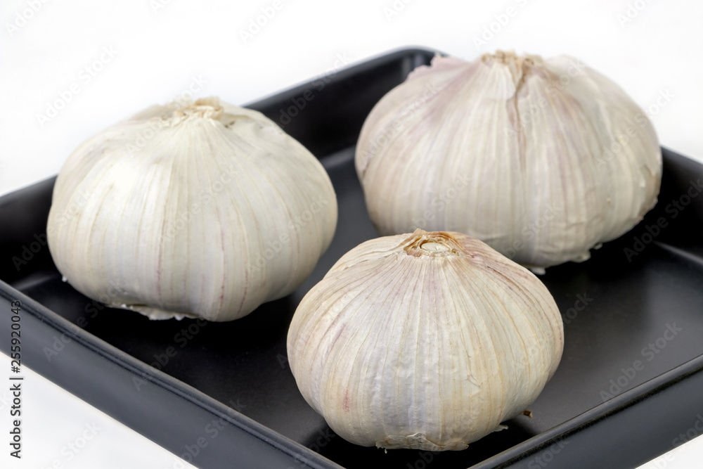 Obraz premium Raw and unpeeled garlic on balck dish on white