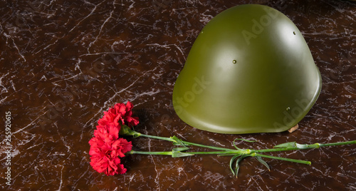 on the marble slab of the monument, there are two carnations and a military headdress, helmet photo