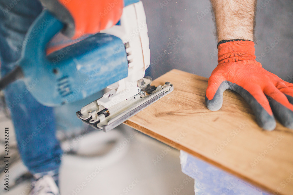 Close-up workplace of laminate laying master - floor boards and electric jigsaw on the floor