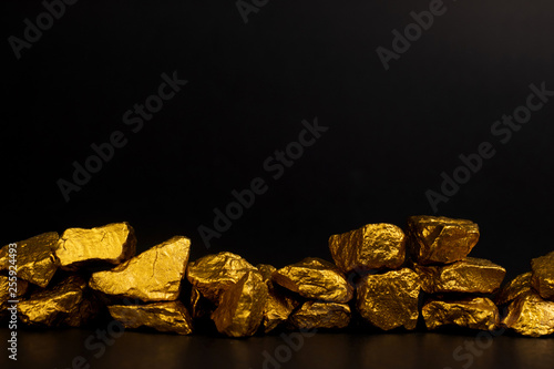 Konstfotografi A pile of gold nuggets or gold ore on black background, precious stone or lump of golden stone, financial and business concept