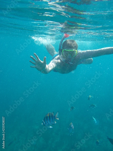 Young man in mask and snorkel dives with fishes. Underwater photo