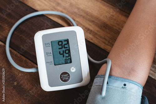 man checking his blood pressure using electronic blood pressure monitor or sphygmomanometer on a wooden table. concept of healthcare, medical instrument and stress management