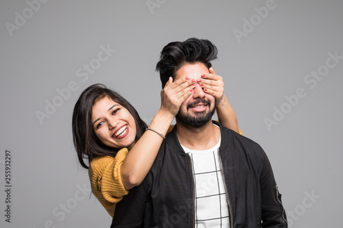Smiling indian girl with her hands covering his eyes guy isolated on gray background © F8  \ Suport Ukraine