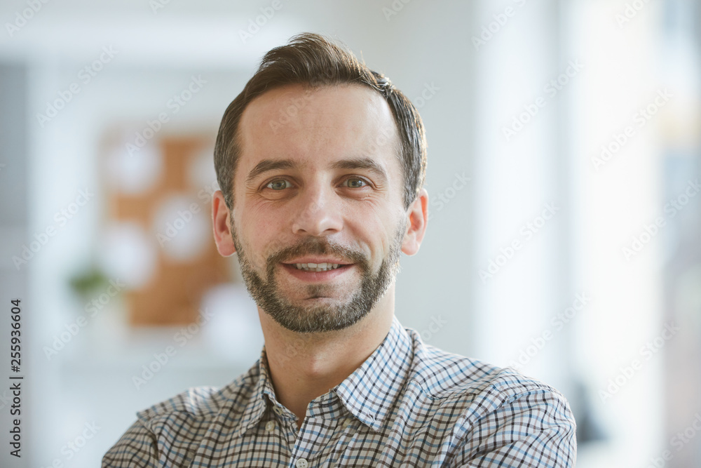 Happy and successful professional in casual shirt looking at you while standing in front of camers in office Happy and successful professional in casual shirt looking at you while standing in front of camers in office